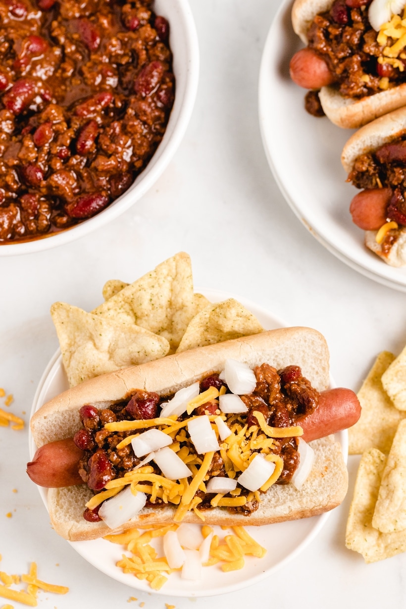 Overhead shot of two chili dogs fully dressed, served with tortilla chips 