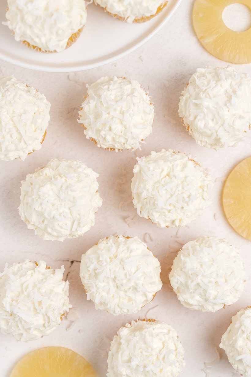 A few Piña Colada Cupcakes displayed together on a plate, highlighting the texture of the whipped cream and golden cupcake base.