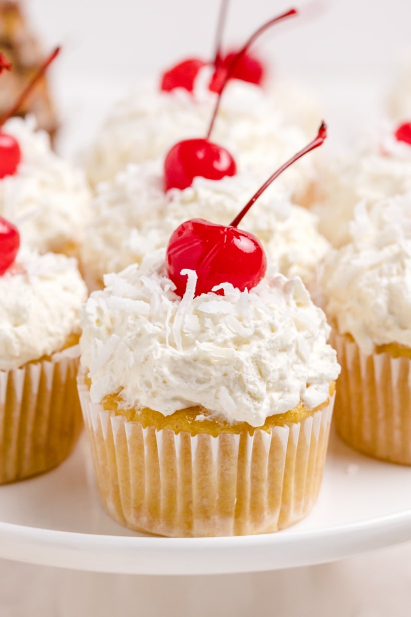 Side view of multiple Piña Colada Cupcakes, showcasing the tropical toppings and creamy whipped frosting.