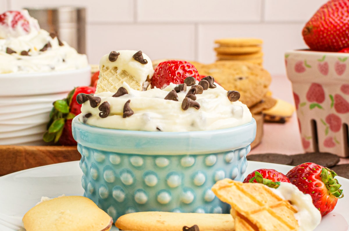 Cannoli dip with strawberry and cookie in blue bowl Cannoli dip in a blue bowl with a strawberry on top, cookie on the side, and styled background elements
