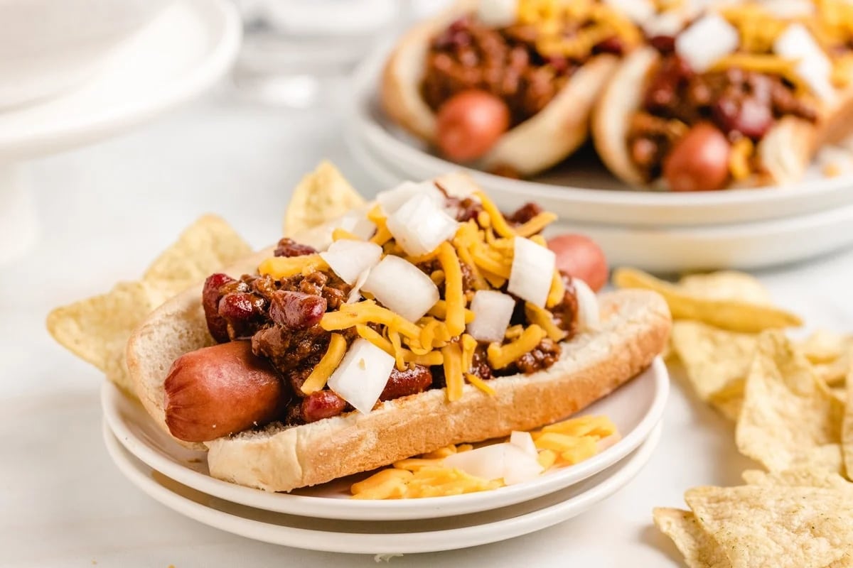 Side view of chili dogs with shredded cheese and onions, served with tortilla chips