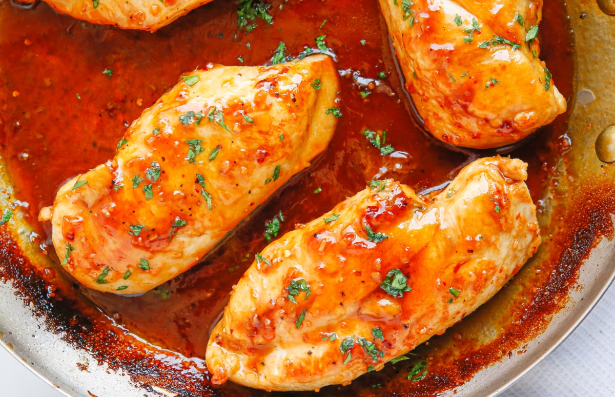 Apricot Glazed Chicken Breasts in sauce Juicy chicken breasts coated in apricot sauce, cooking in a skillet.