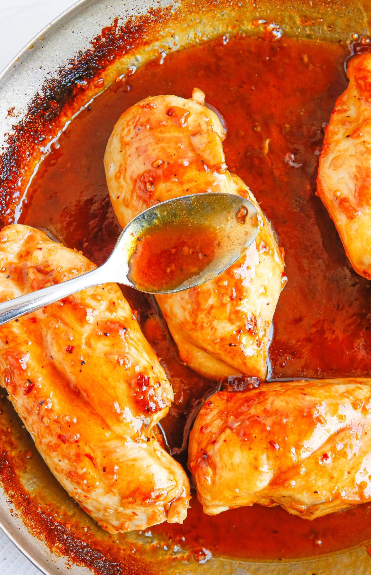 Apricot Glazed Chicken Breasts in simmering sauce A spoon drizzling thick apricot sauce over a golden-brown chicken breast in the skillet.