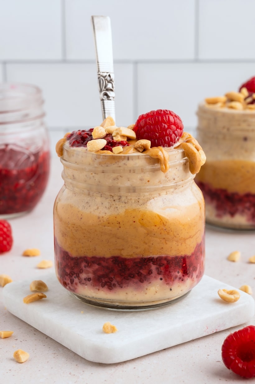 Peanut Butter and Jelly Overnight Oats with a spoon Jar of Peanut Butter and Jelly Overnight Oats topped with peanut butter and raspberry jam