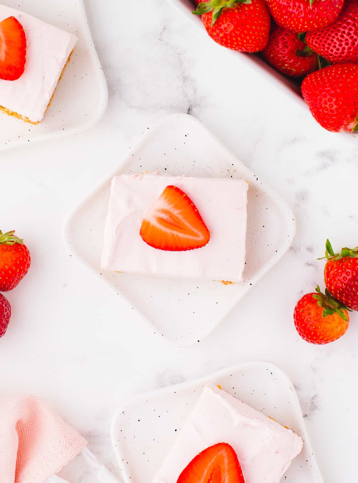 Overhead shot of three no-bake strawberry cheesecake bars on a white surface