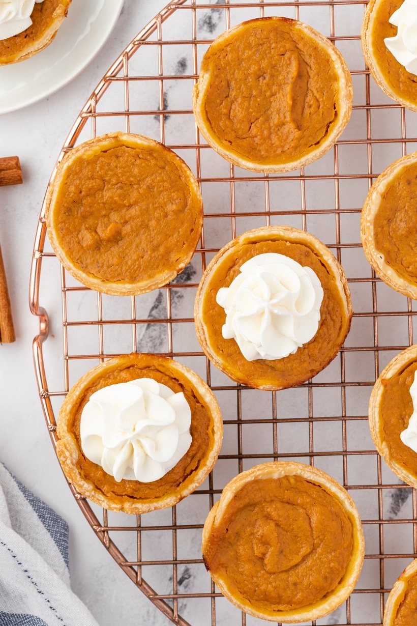 Cooling Mini Pumpkin Pies After Baking Mini pumpkin pies cooling on a rack, some topped with whipped cream and others plain.