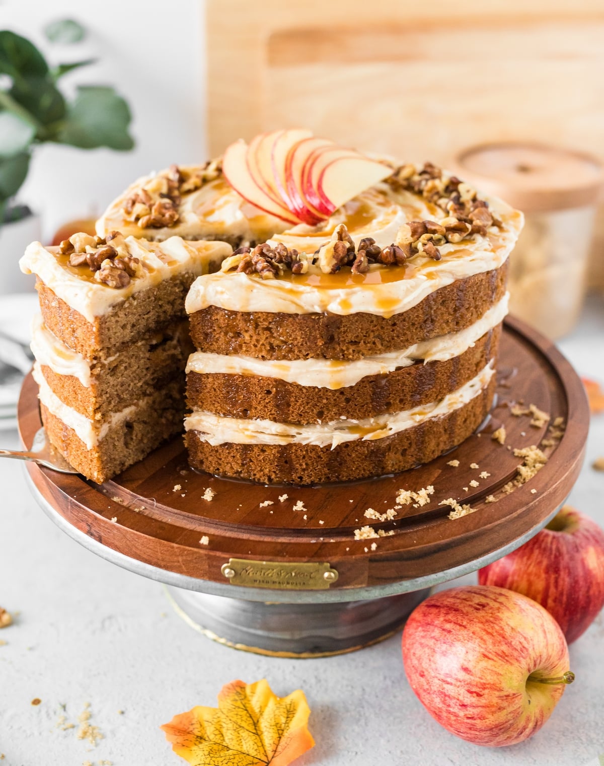 Serving Caramel Apple Layer Cake Full view of a caramel apple layer cake on a cake stand, with a slice being removed, revealing its layers.