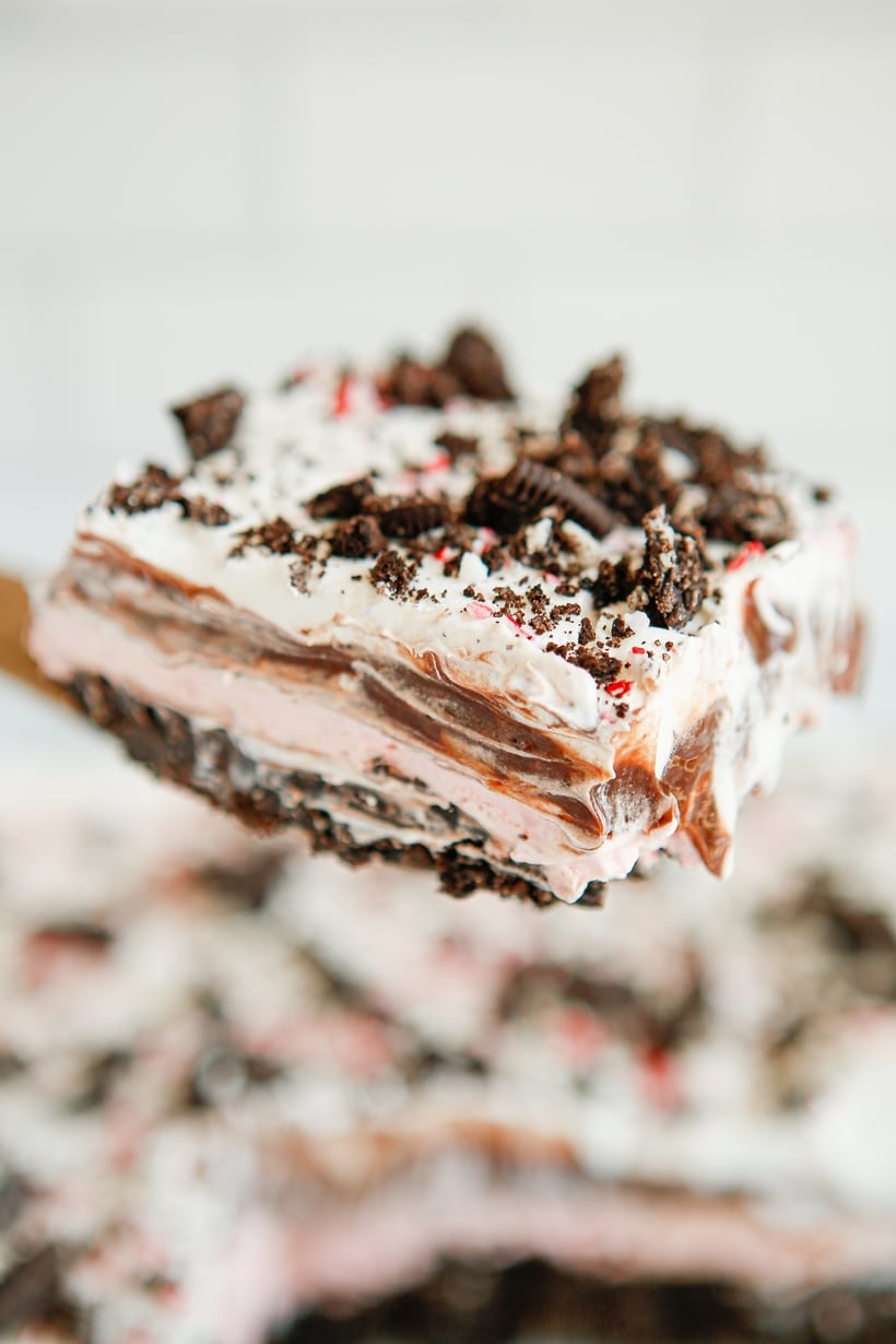 Layered Slice of Chocolate Peppermint Lush on a Spatula A slice of chocolate peppermint lush with visible layers of Oreo crust, creamy peppermint, chocolate pudding, and whipped topping, held on a spatula.