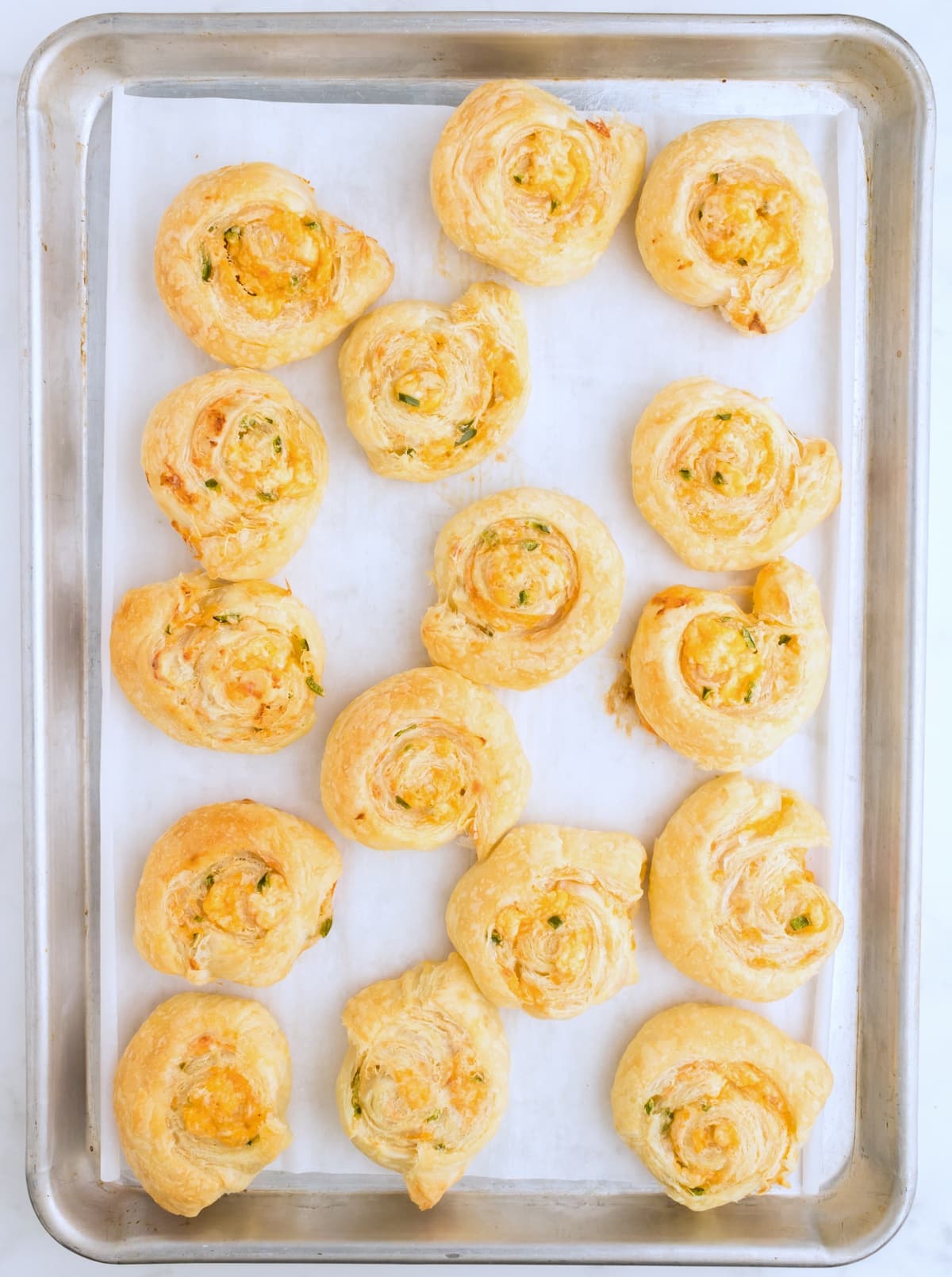 Jalapeno Popper Pinwheels on a baking sheet Close-up of Jalapeño Popper Pinwheels on a baking sheet, showing their golden brown puff pastry and melted cheese inside.