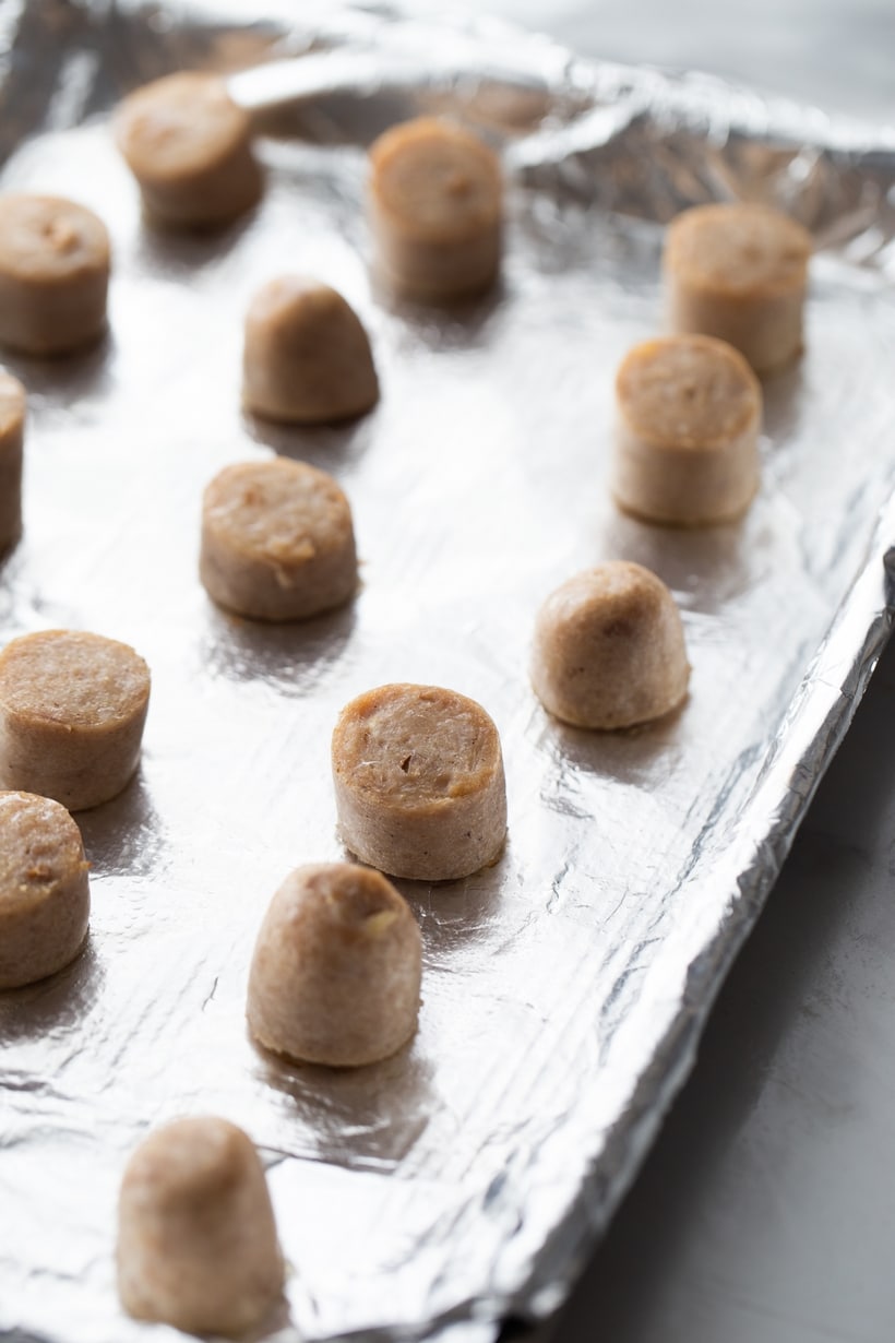 Sliced chicken sausage pieces arranged on a rimmed baking tray, ready to bake.