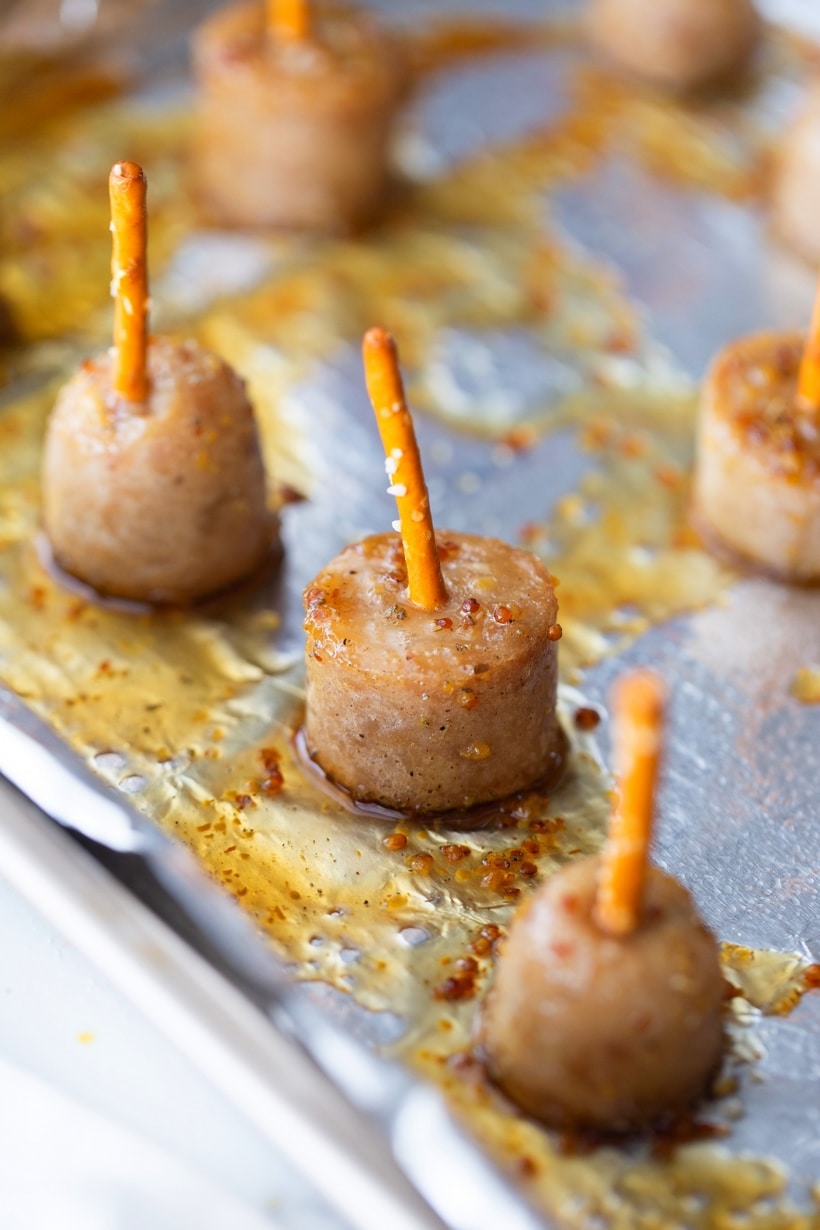 Maple-glazed sausage bites skewered with pretzel sticks on a baking tray, ready to serve.