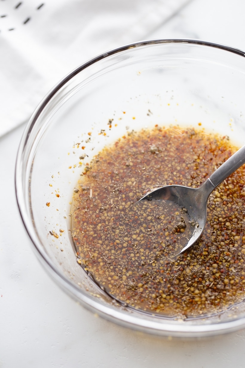 A bowl of maple syrup, mustard, and crushed sage being stirred together to make a savory glaze.