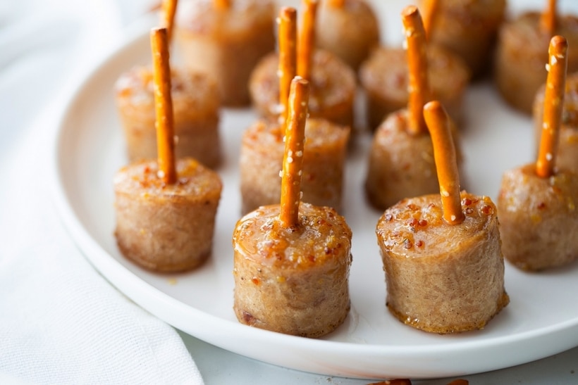 sMaple-glazed sausage bites skewered with pretzel sticks arranged on a white platter.