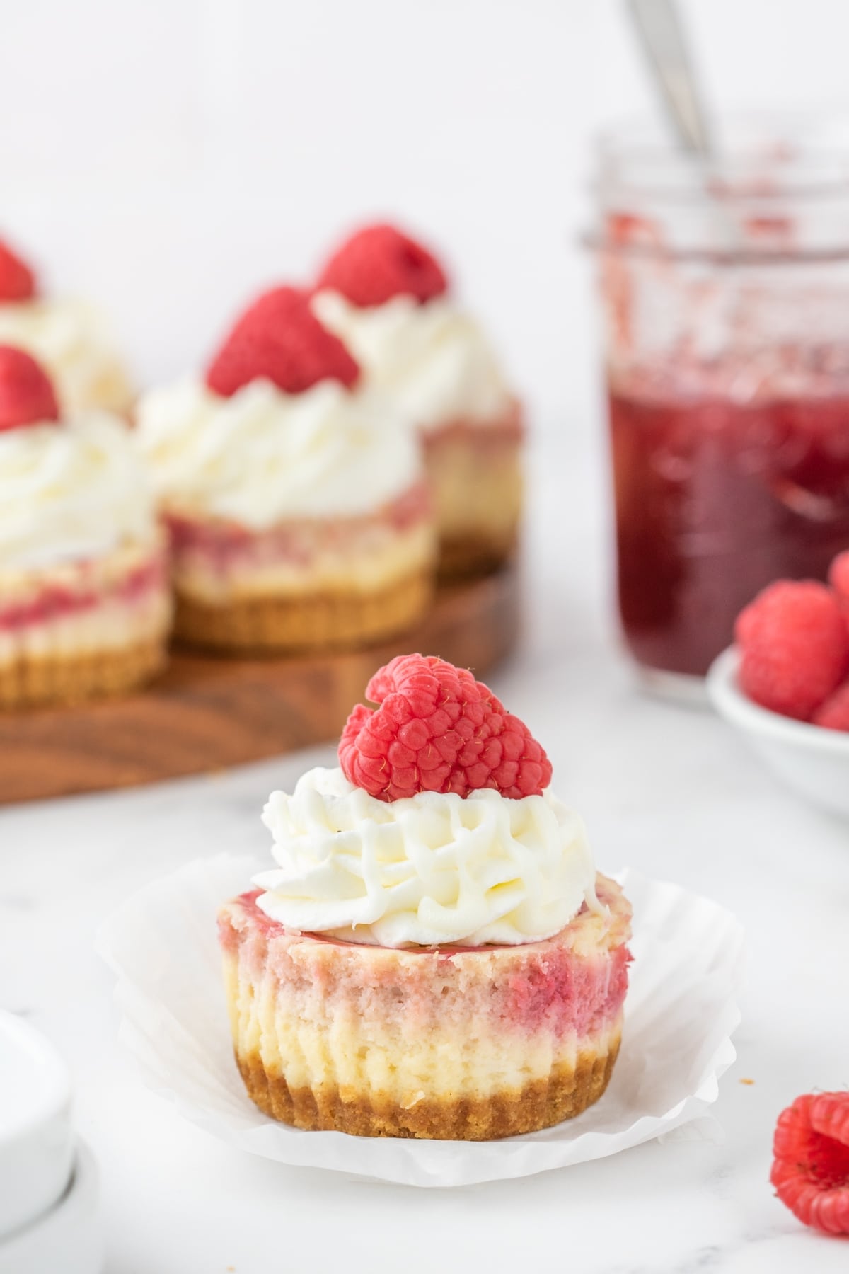 Overhead close-up of a mini cheesecake with raspberry swirl and white chocolate drizzle detail.