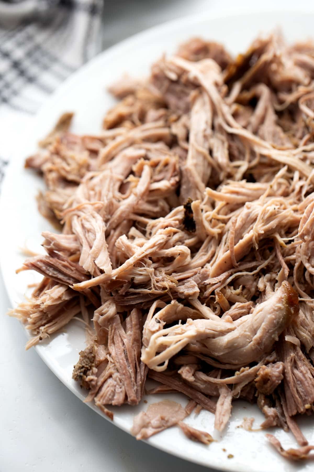 Cooked pork shredded on a white plate, ready to go back into the slow cooker