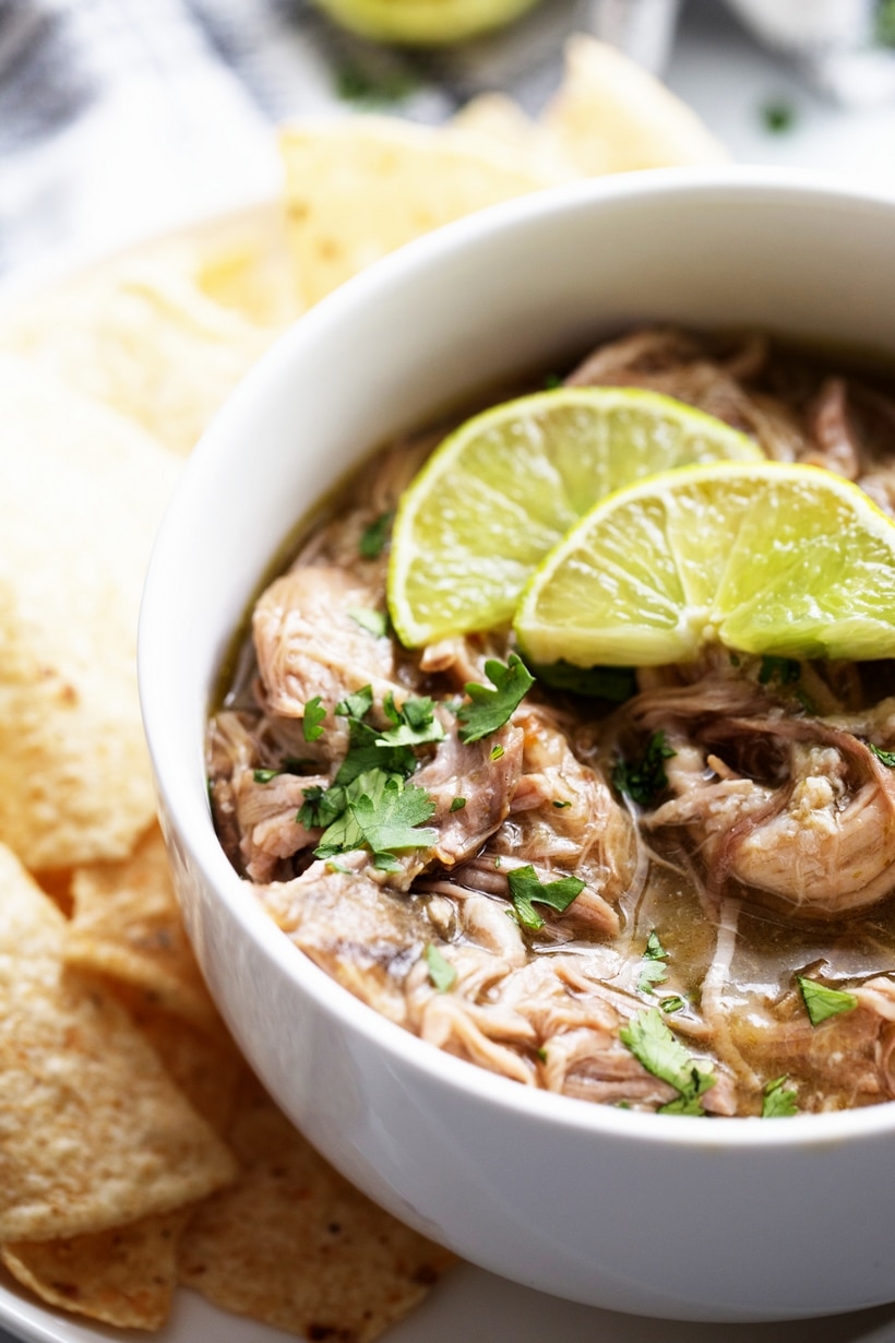 Slow cooker pulled pork chile verde served in a white bowl with lime slices on top 