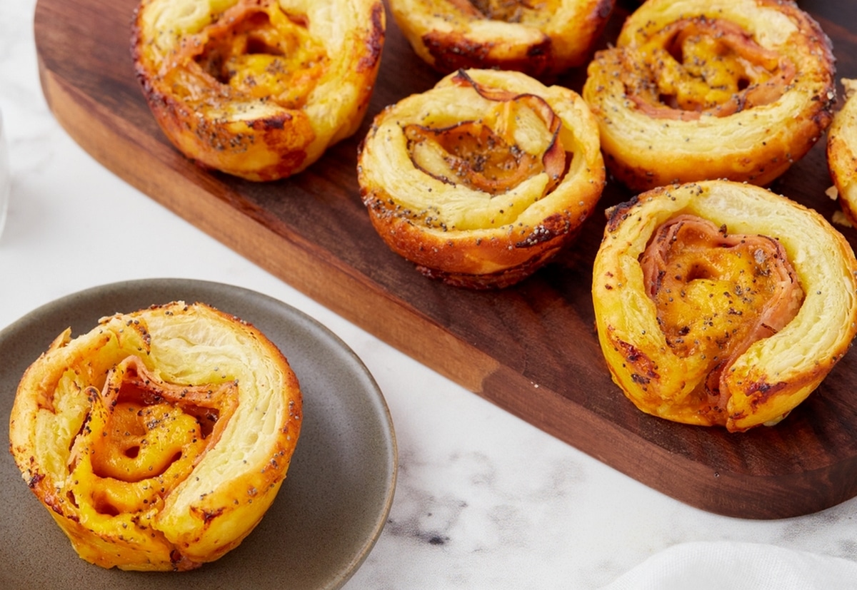 Ham and Cheese Pinwheels on a cutting board. Flaky puff pastry rolls filled with ham and melted cheese, ready to serve.
