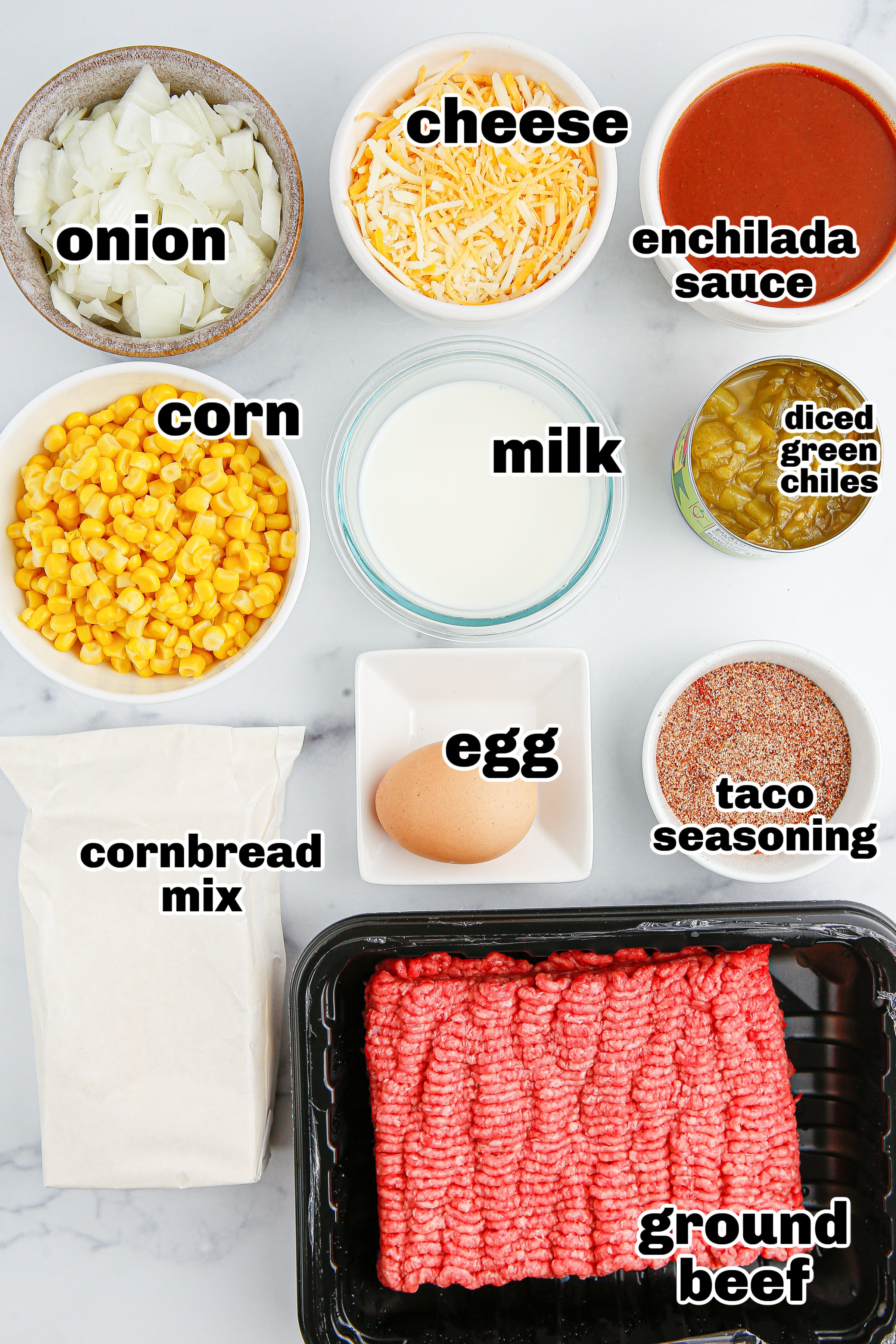 All the ingredients laid out, including ground beef, taco seasoning, corn, enchilada sauce, green chilies, cheese, and Jiffy cornbread mix.