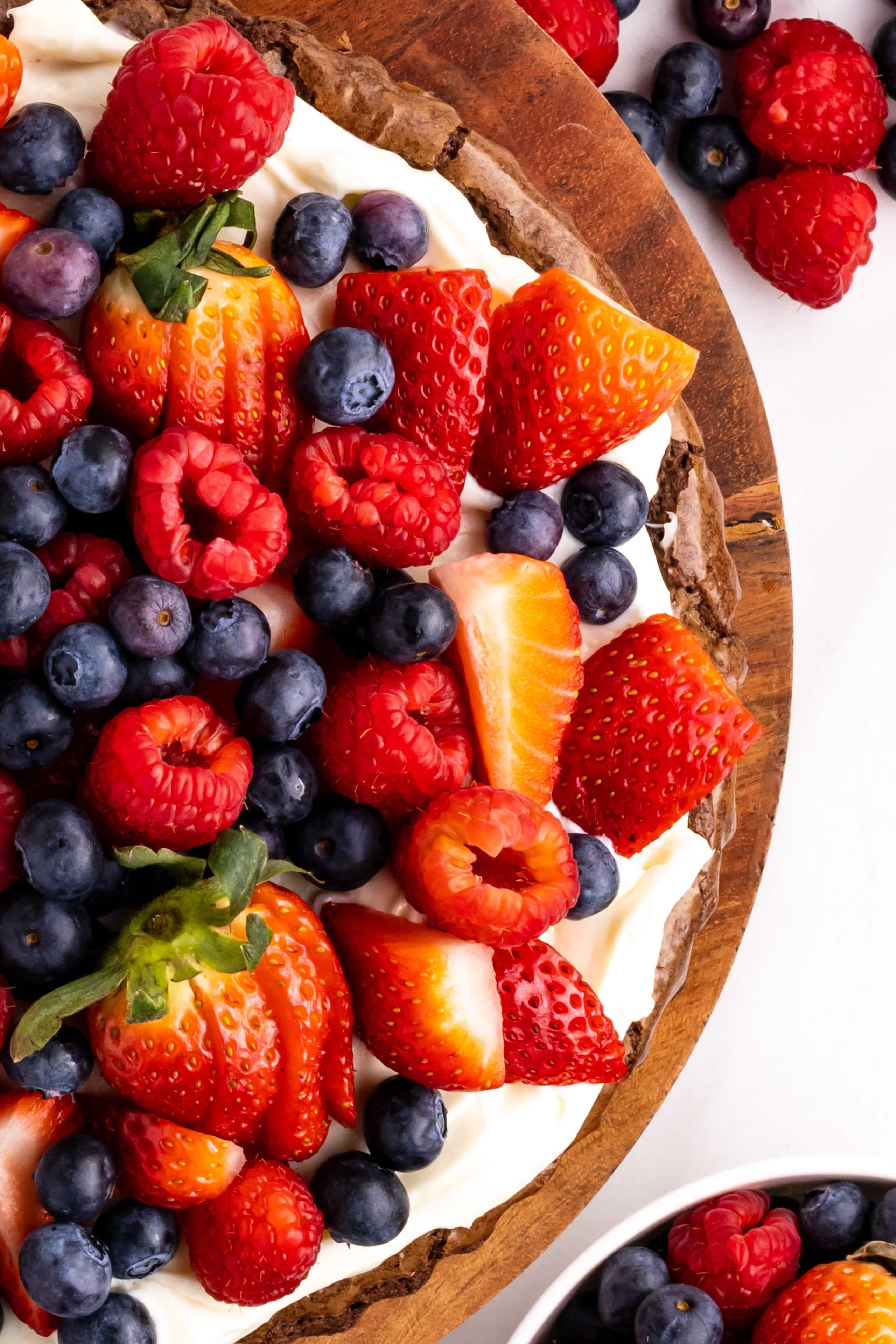Close-up of brownie fruit pizza with cream cheese frosting and fresh berries on top.