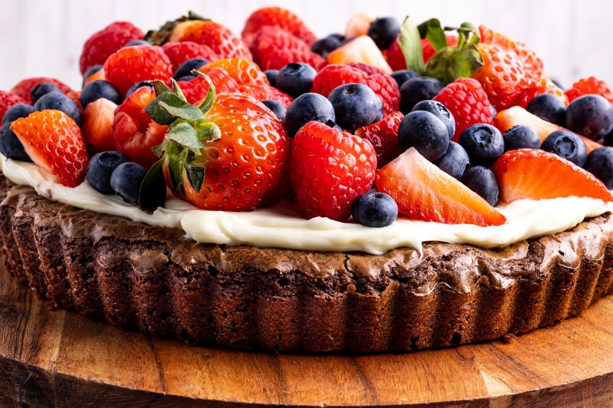Side view of chocolate brownie pizza topped with cream cheese frosting and fruit