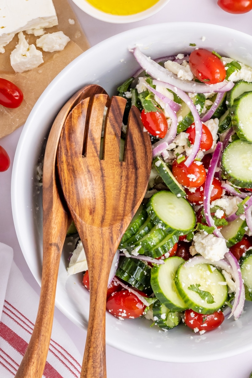 Cucumber Salad with Feta Cheese and Olive Oil Bowl of cucumber red onion feta salad with wooden serving spoons, shown next to a block of feta and olive oil.