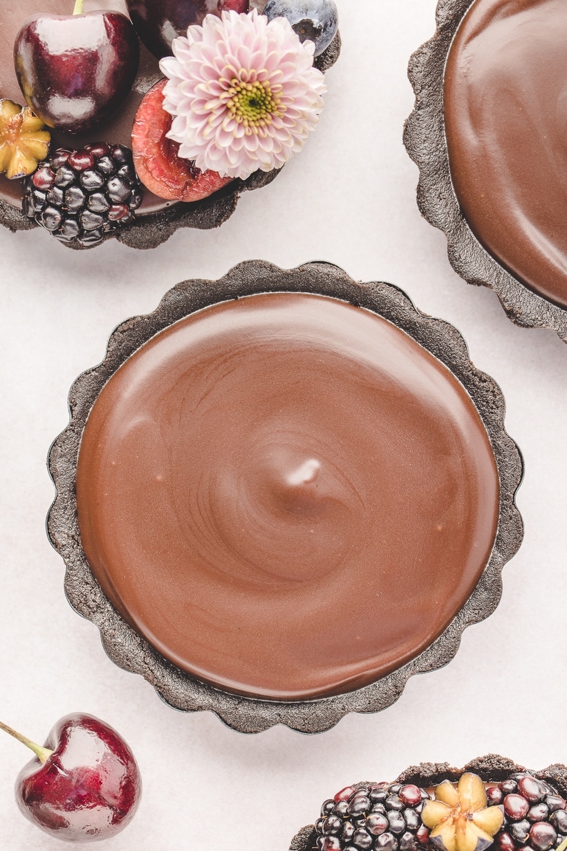 Overhead view of a plain mini chocolate ganache tart with a glossy, smooth ganache top and no toppings.