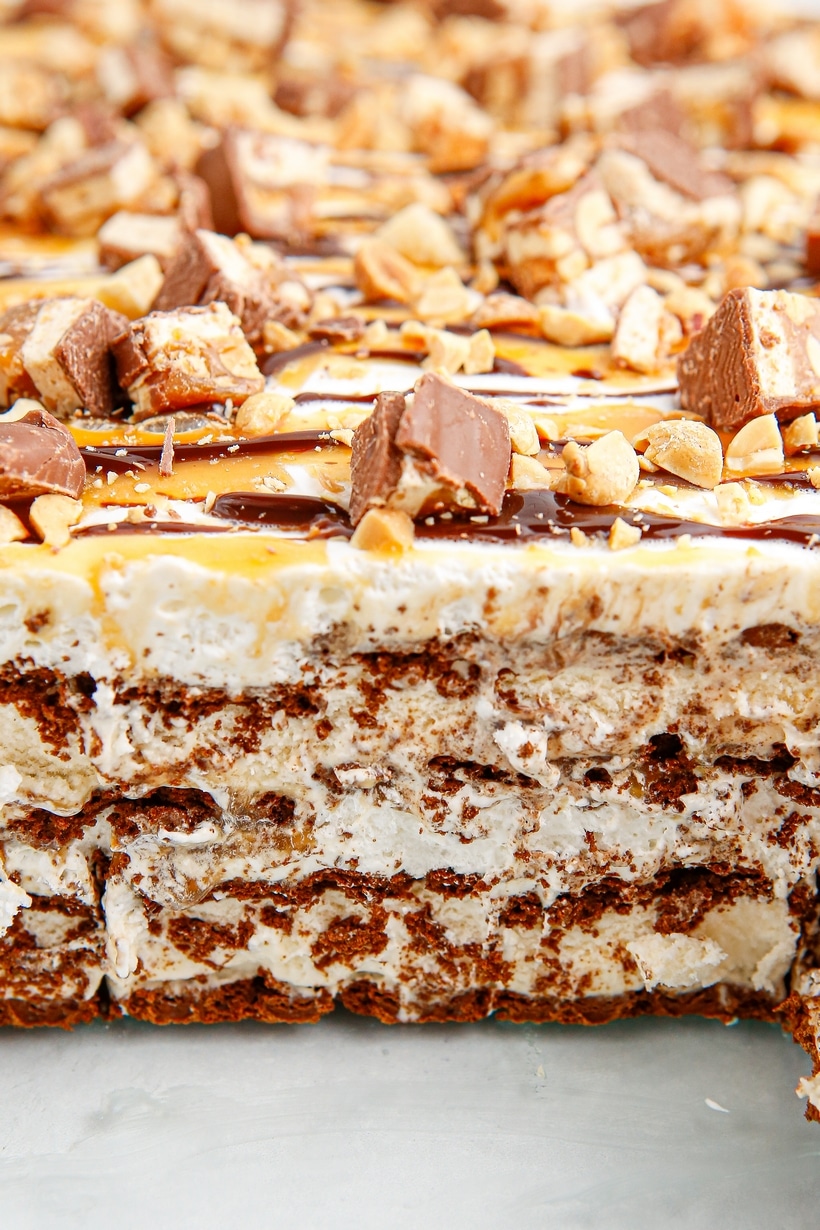 snickers ice cream cake cross section with layers of sandwiches and toppings Close-up of layered snickers ice cream sandwich cake with chopped candy bars, peanuts, caramel, and chocolate drizzle
