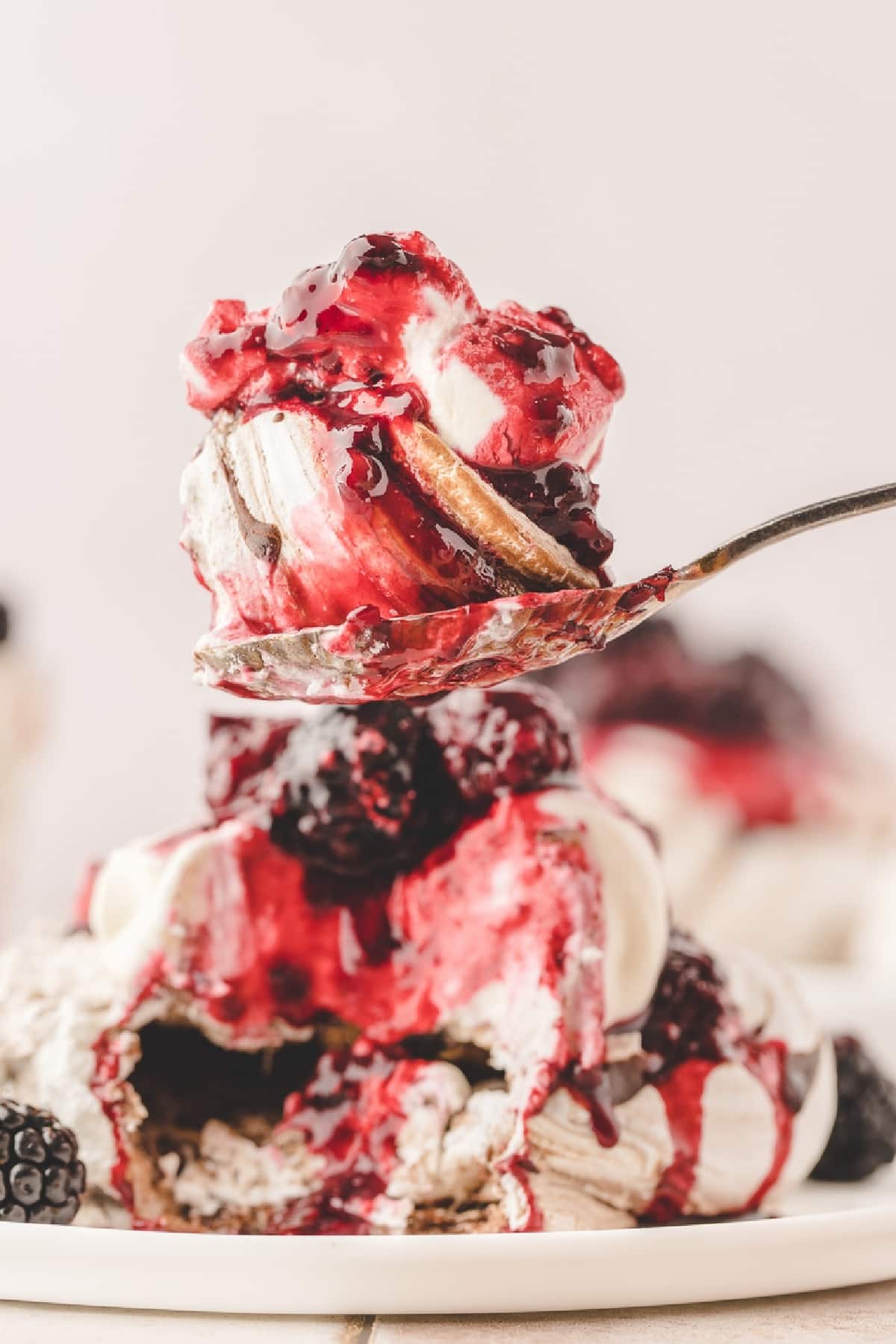 Spoonful of chocolate blackberry pavlova with whipped cream, blackberry compote and fresh blackberries.