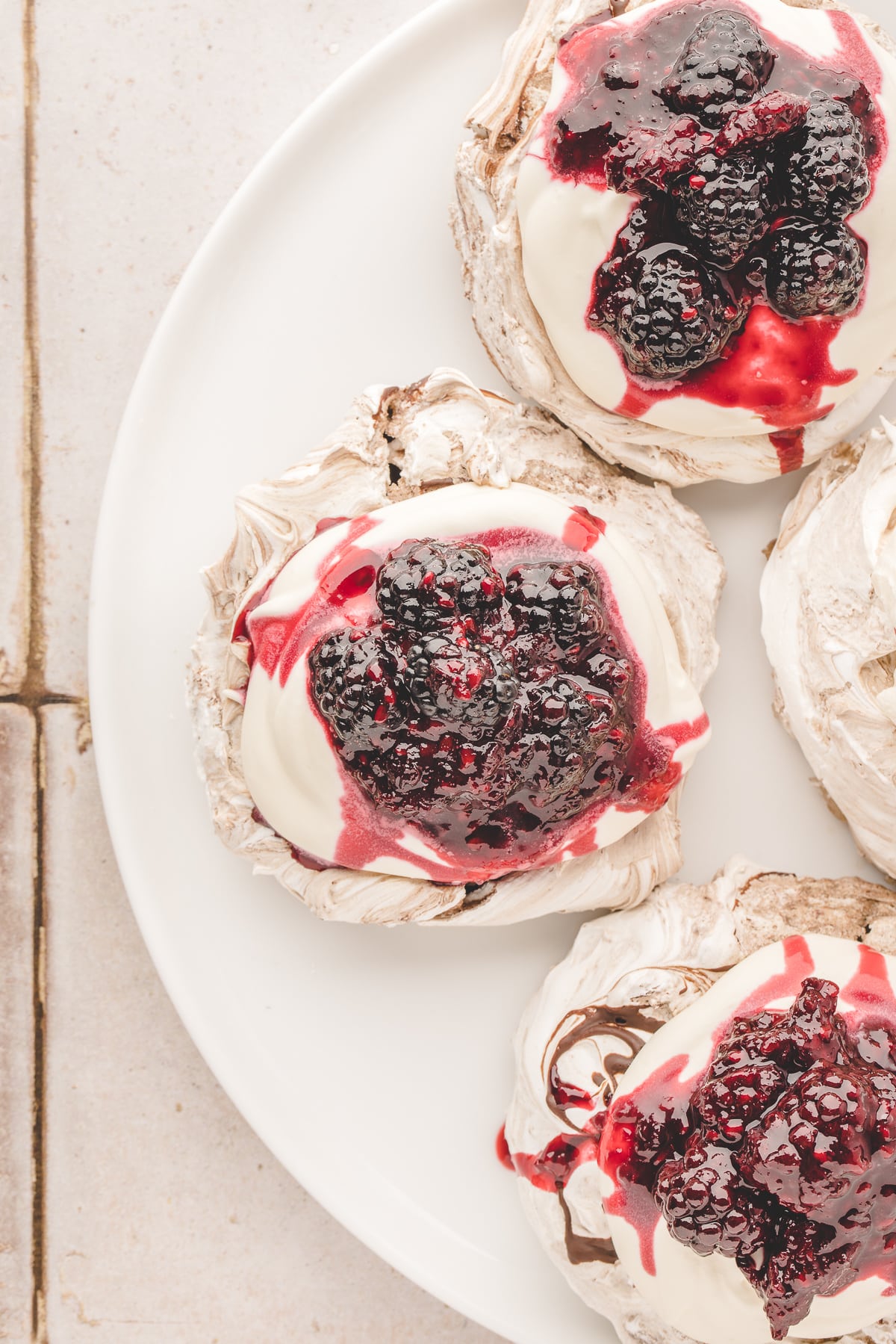 Individual chocolate-swirled pavlova topped with soft whipped cream, fresh blackberries and blackberry compote.