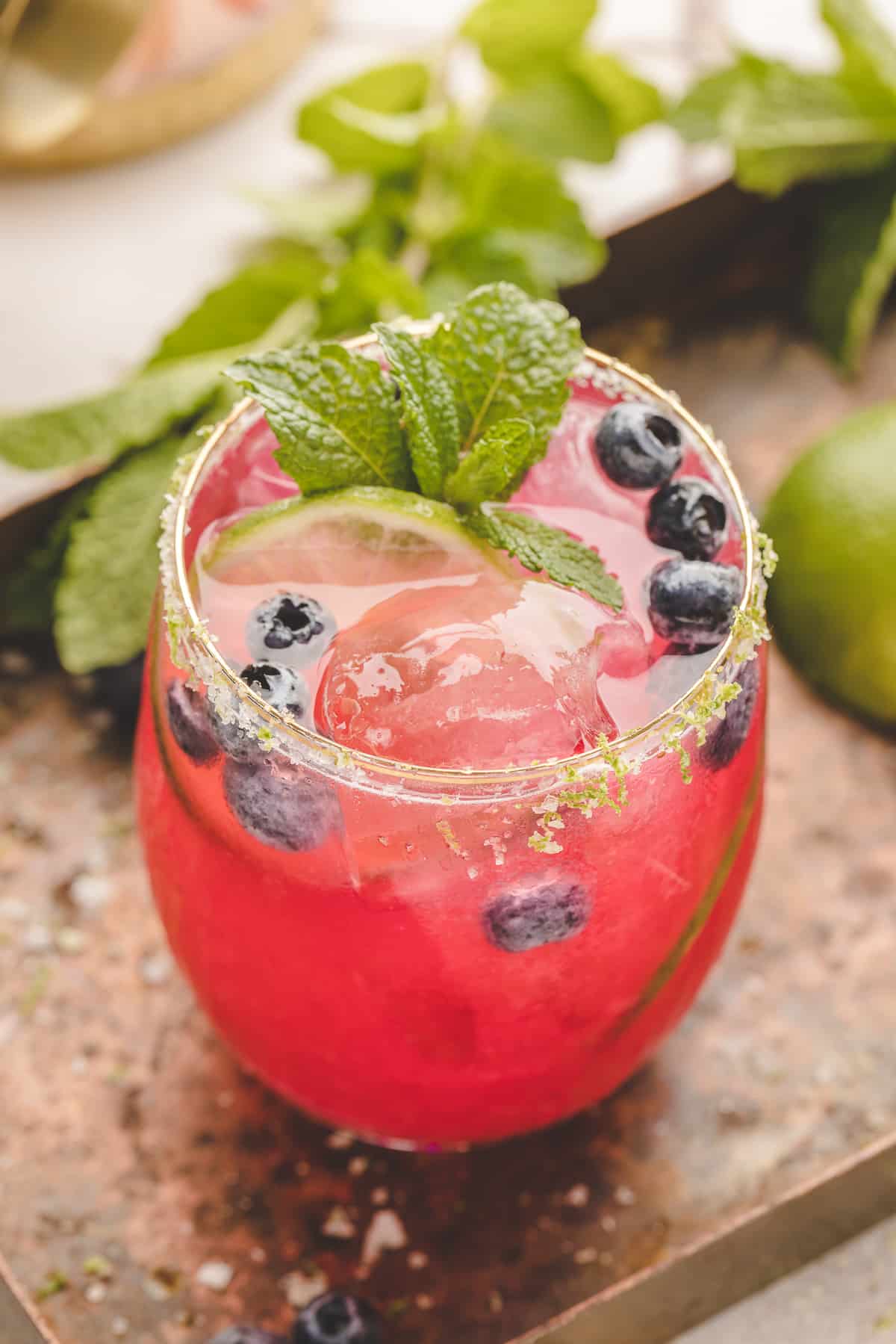 A vibrant blueberry margarita served on the rocks with a lime salt rim, fresh blueberries, and a mint sprig.