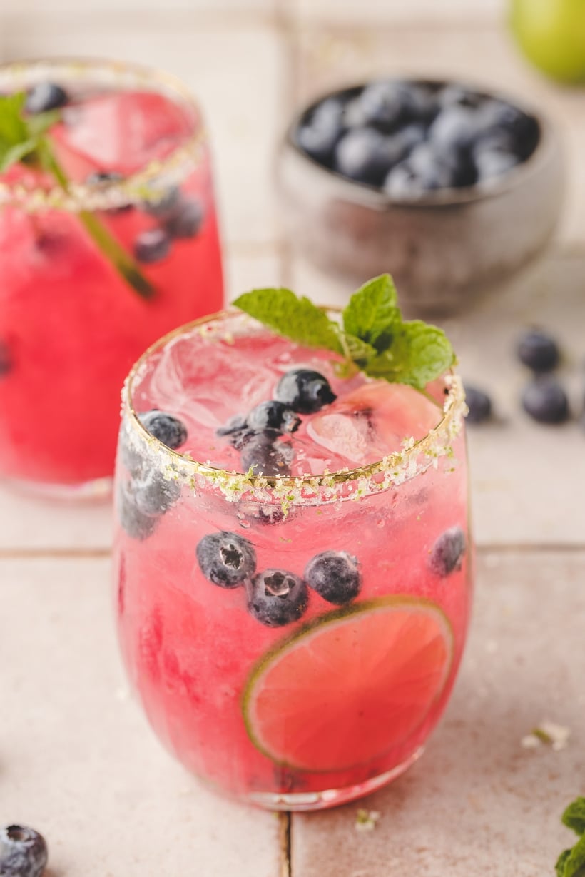 Fresh blueberries fully muddled in the bottom of a shaker, releasing their juices.