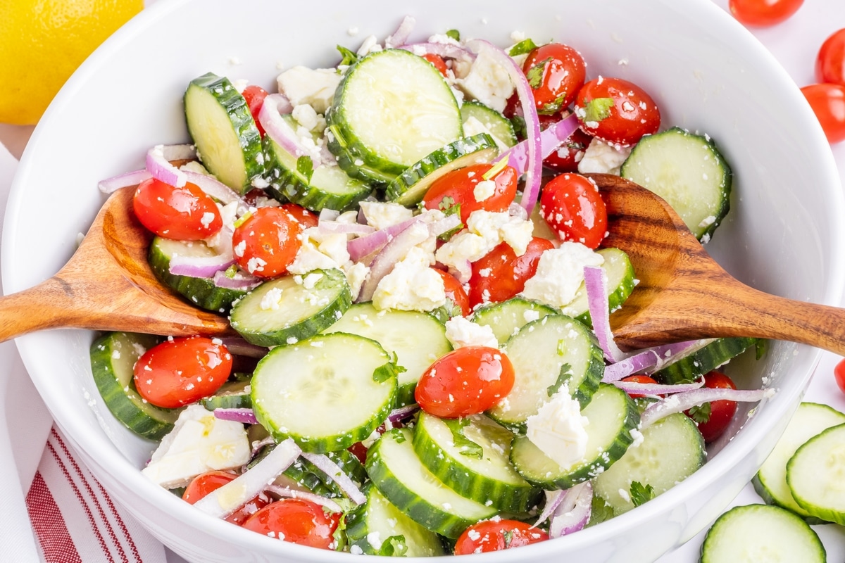Cucumber Feta Salad with Red Onion and Lemon Dressing Overhead view of cucumber feta salad in a white bowl with tomatoes, red onion, and fresh herbs tossed in lemon dressing.