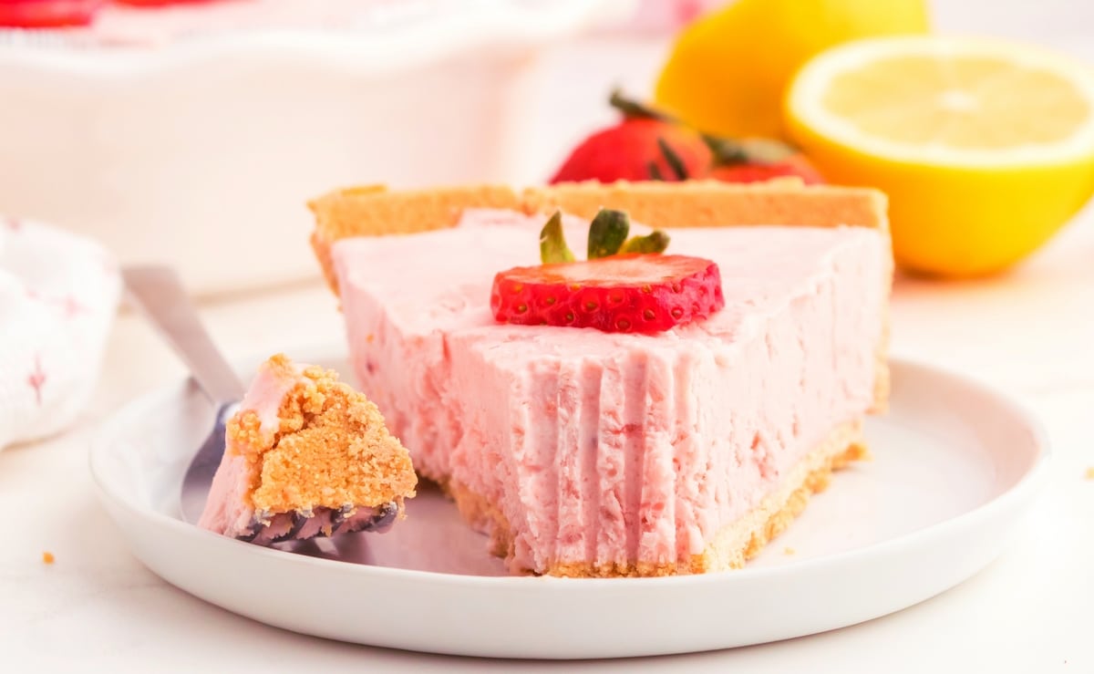 strawberry lemonade pie slice with bite missing and lemons behind Pie slice with a bite taken out and lemons in the background