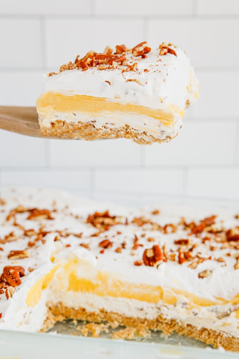 Serving Pecan Cream Pie Lush from Baking Dish Wooden spatula lifting a slice of Pecan Cream Pie Lush from the baking dish, displaying the dessert's layers and texture.