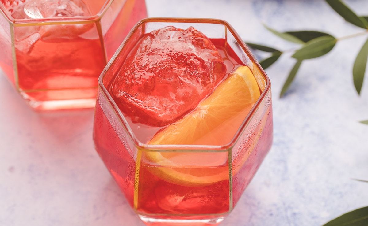 Two Negronis with ice and orange wedge garnish Two Negroni cocktails on the rocks, each served with an orange wedge garnish.