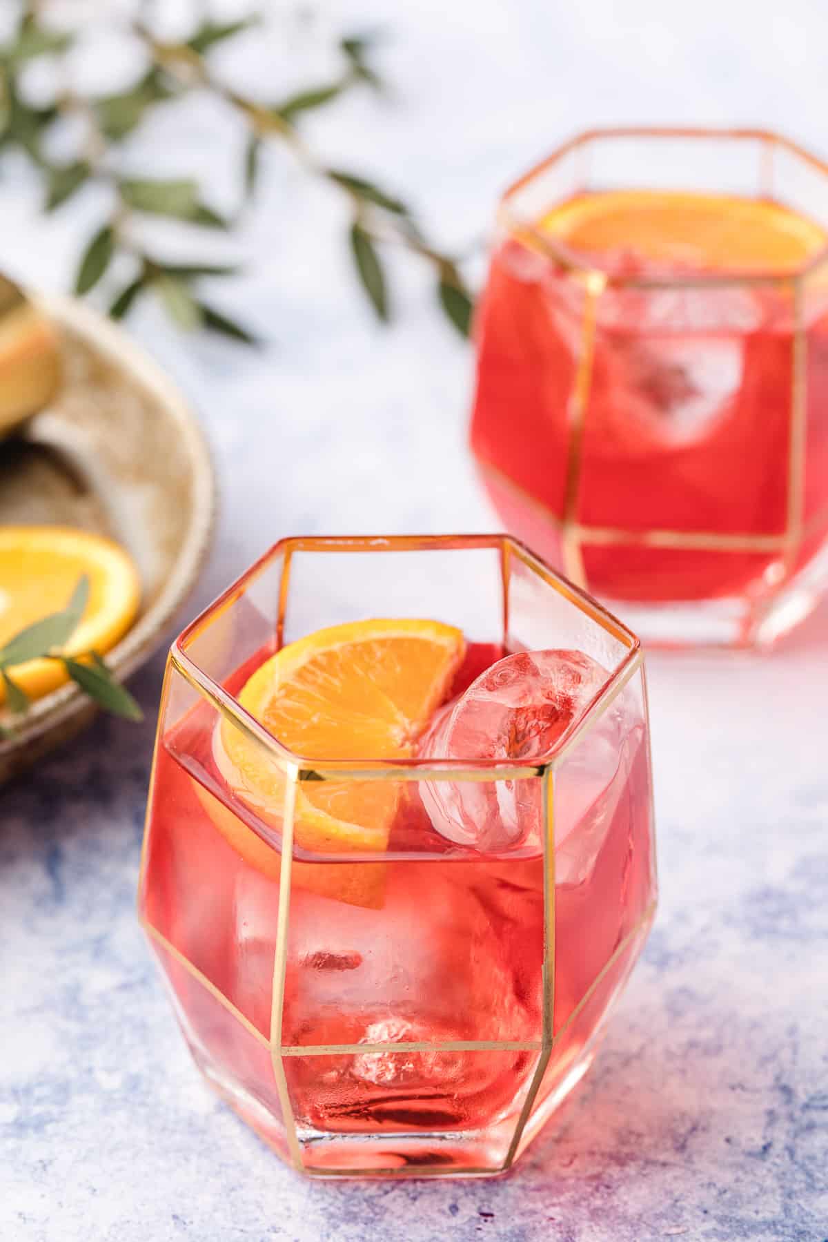Negroni cocktails with garnish and olive branch detail Less bitter Negroni cocktails served over ice with orange peel, styled with olive branches.