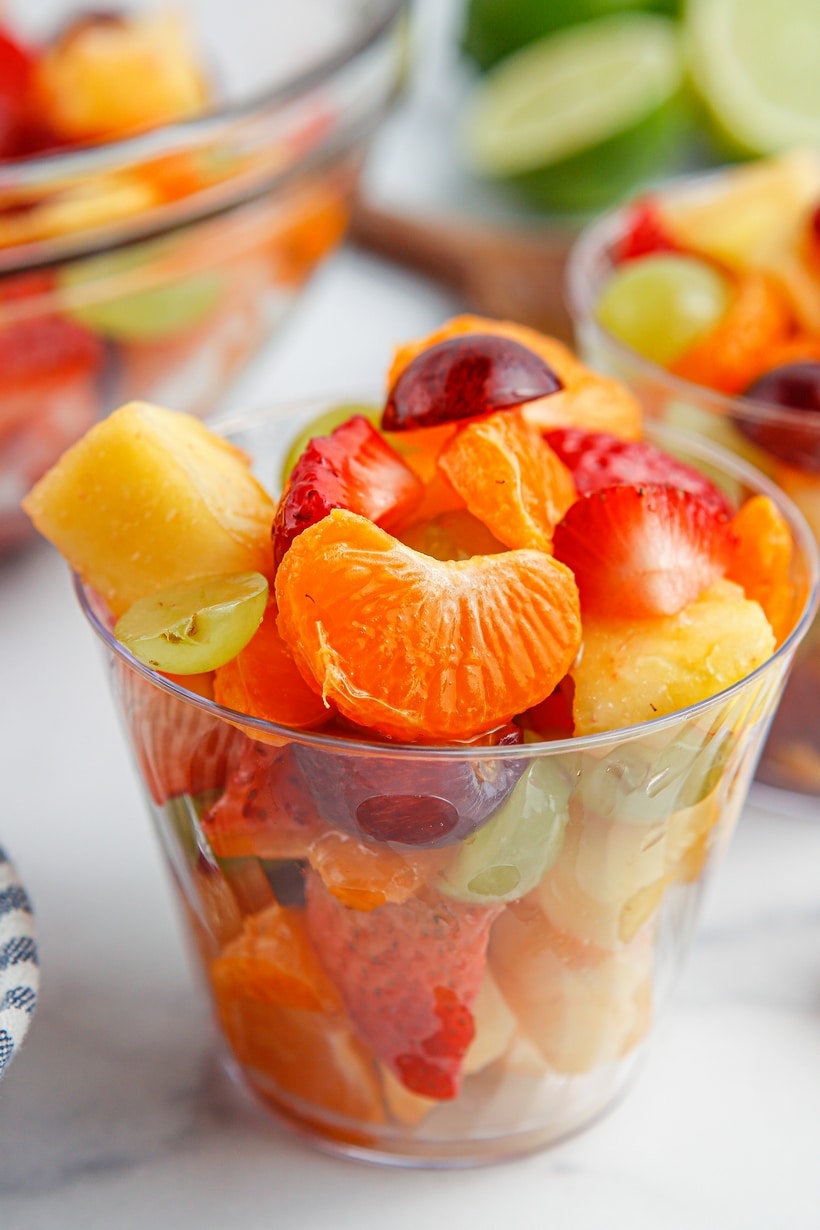 a cup of Honey Lime Fruit Salad Tight shot of a clear cup filled to the top with honey lime fruit salad, emphasizing the glossy glaze and freshness of each fruit piece.