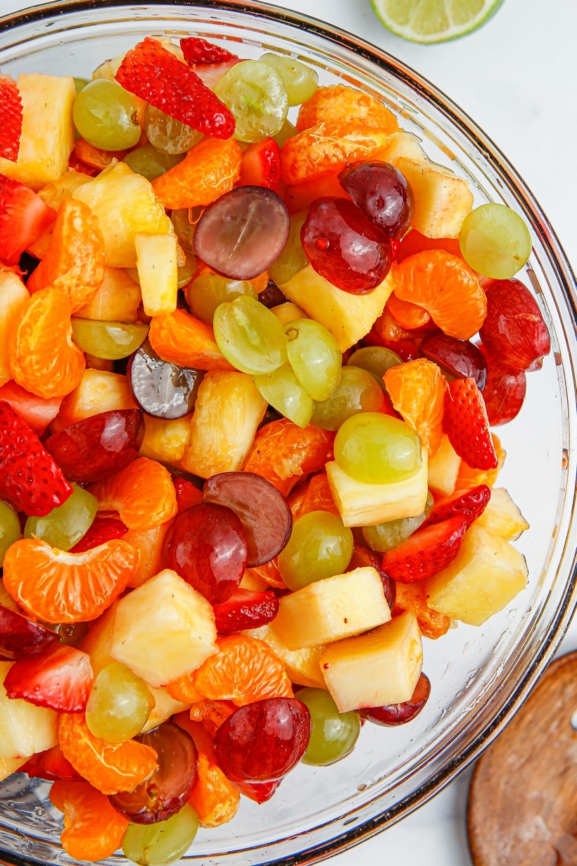 Honey Lime Fruit Salad in a mixing bowl Overhead shot of a large bowl filled with honey lime fruit salad, showing vibrant colors from grapes, pineapple, strawberries, and clementines.