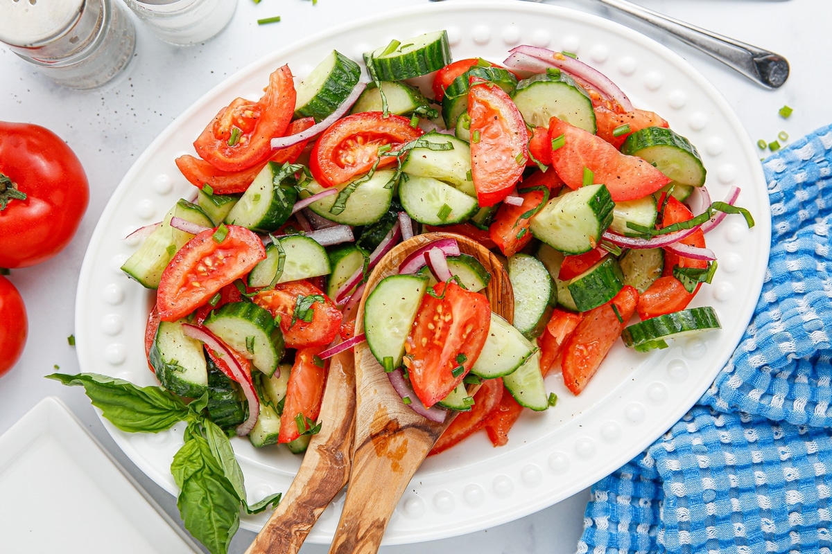 Overhead view of cucumber tomato onion salad served on a white platter with wood serving utensils