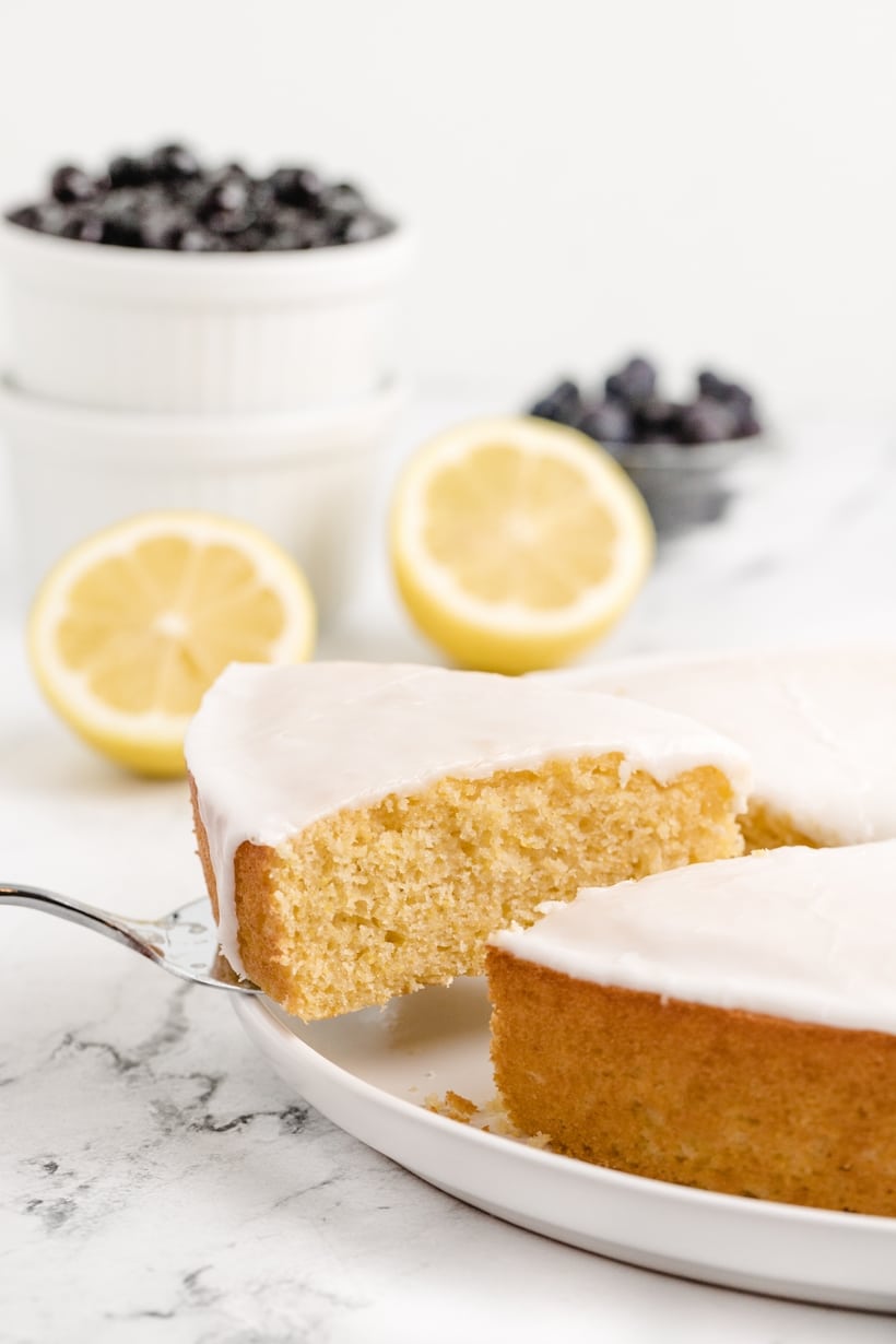 removing a slice of Lemon Cornmeal Cake A slice being lifted from the whole glazed cake, showing the soft interior.