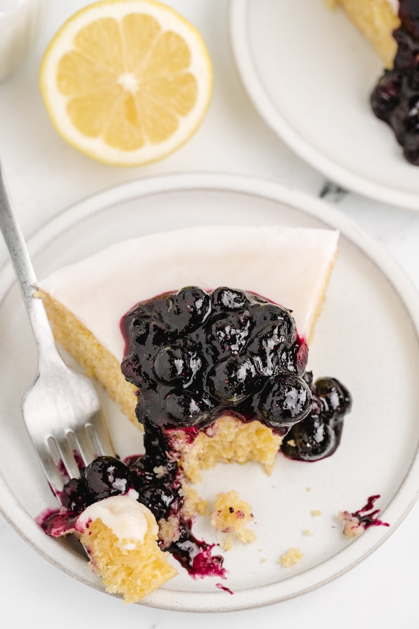 taking a bite of lemon cornmeal cake Top view of a plated slice with blueberry sauce and a fork resting beside it, a bite taken.