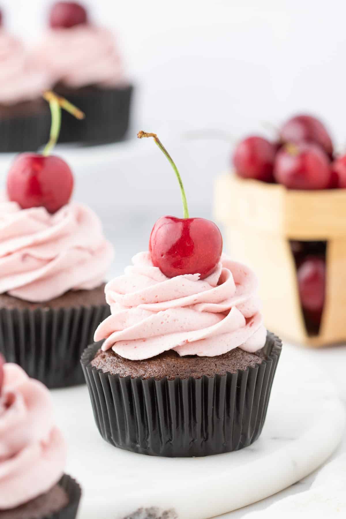 Chocolate cherry cupcakes arranged on a white marble serving platter with cherry buttercream and fresh cherries on top.