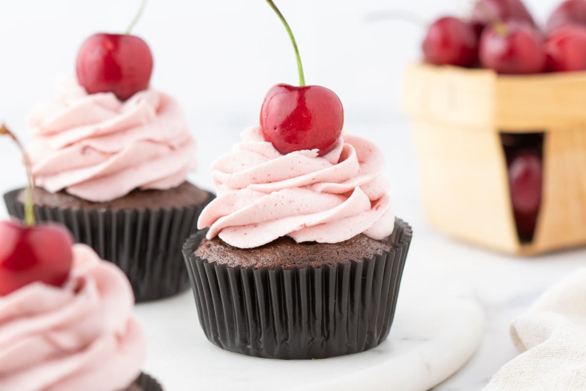 Single chocolate cherry cupcake with cherry buttercream frosting, shown from the front on a white marble surface.