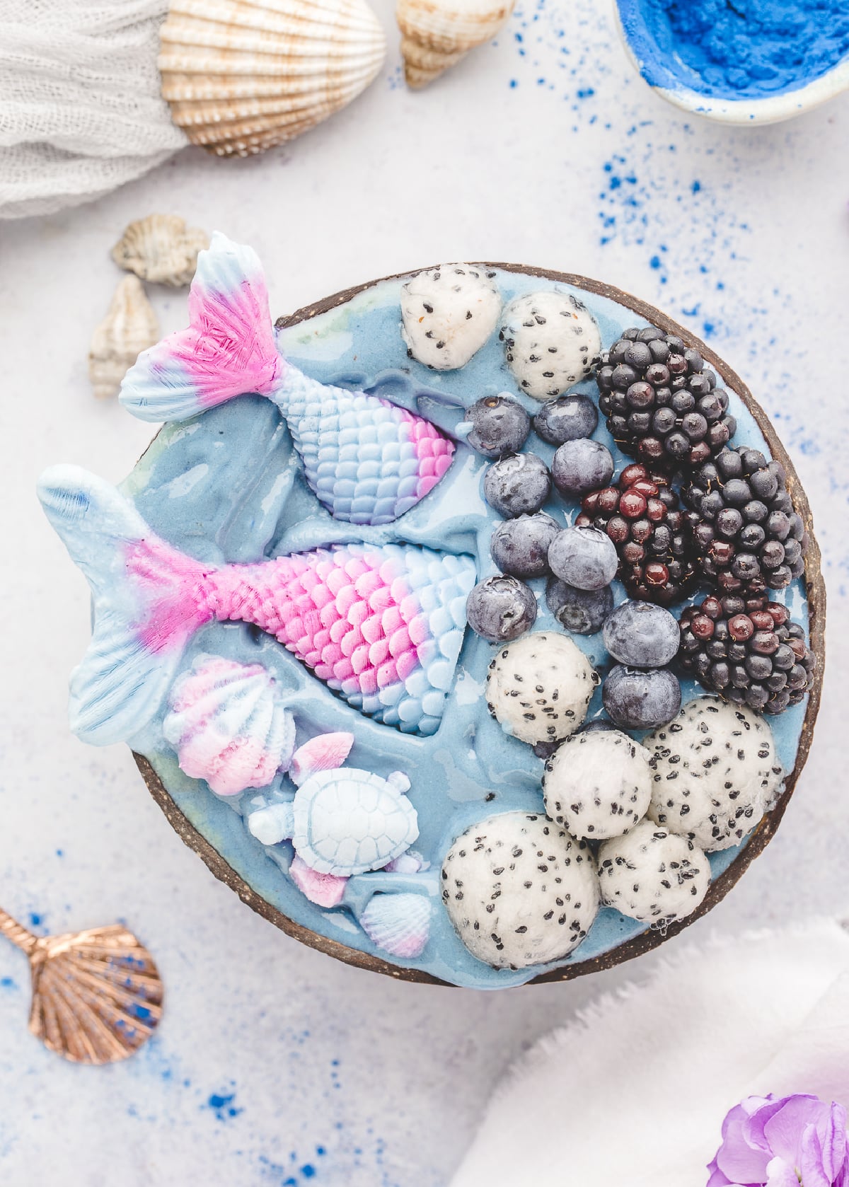 Mermaid smoothie bowls with homemade yogurt mermaid tails and fresh fruit. Mermaid smoothie bowls topped with yogurt mermaid tails, dragon fruit, blueberries, and blackberries in a coconut bowl.