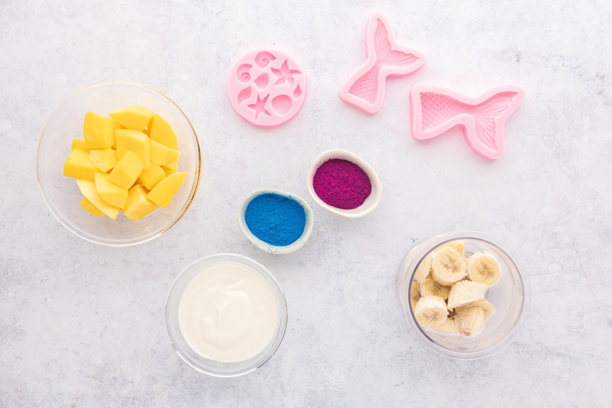 Everything you need to make mermaid smoothie bowls and colorful yogurt mermaid tails. Ingredients for mermaid smoothie bowls including frozen bananas, mango, yogurt, blue spirulina powder, beet root powder, and silicone mermaid molds.