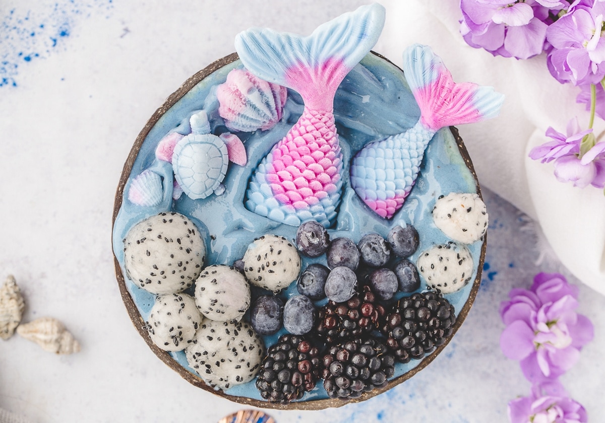 An overhead look at colorful mermaid smoothie bowls ready to serve. Overhead view of mermaid smoothie bowls topped with yogurt mermaid tails, dragon fruit, blueberries, and blackberries.