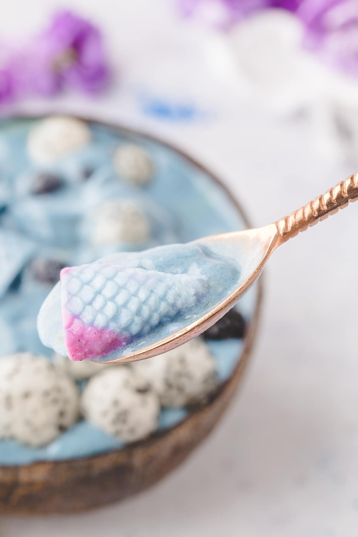 A spoonful of smoothie with a colorful yogurt mermaid tail. Close-up of a spoon holding a yogurt mermaid tail with a blue smoothie in the background.
