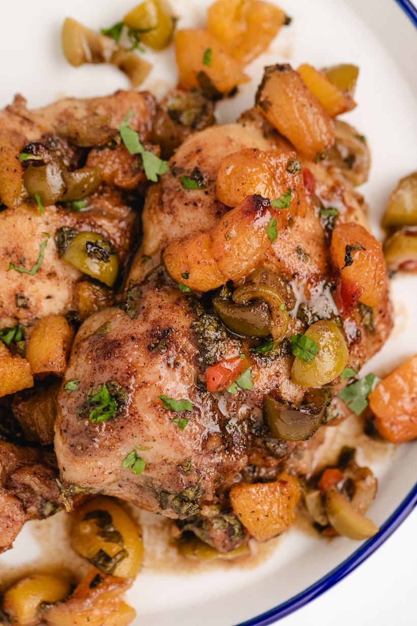 close view of apricot chicken thighs with olives Close-up of baked apricot chicken thighs covered in spiced pan sauce, olives, and apricot pieces.