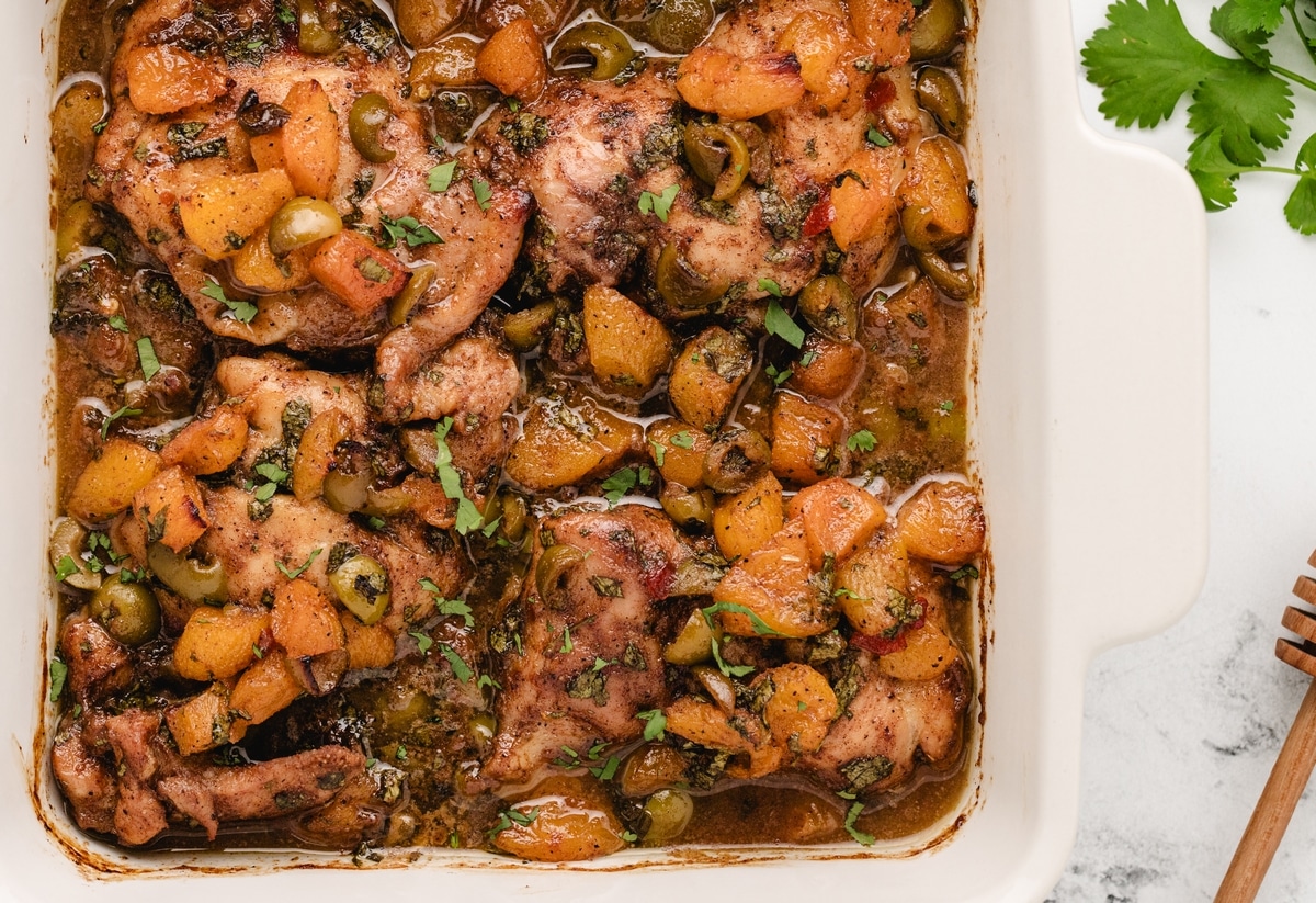 oven baked chicken thighs with apricots and olives in baking dish Baking dish filled with marinated chicken thighs, olives, and softened dried apricots in a glossy sauce.