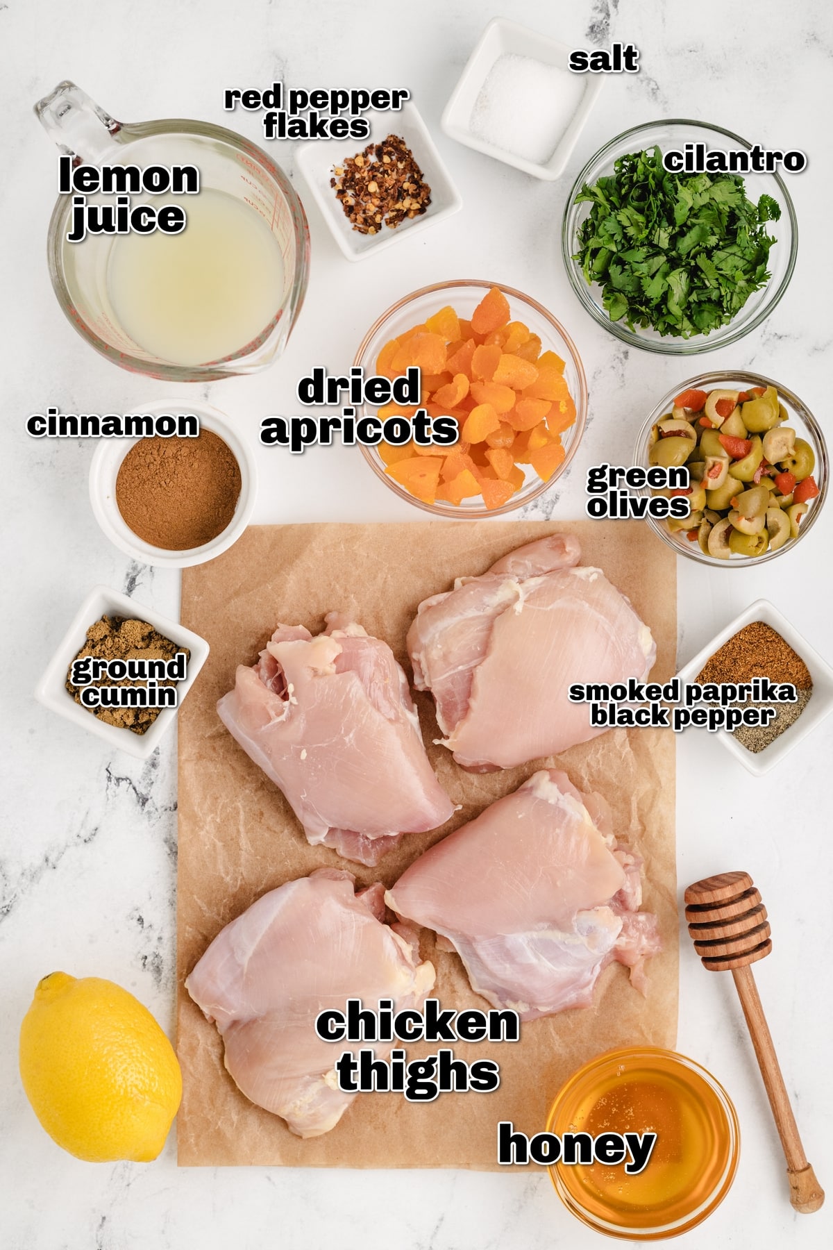 ingredients for apricot chicken thighs labeled overhead Overhead of labeled ingredients for apricot chicken thighs, including chicken, lemon juice, dried apricots, olives, and spices.
